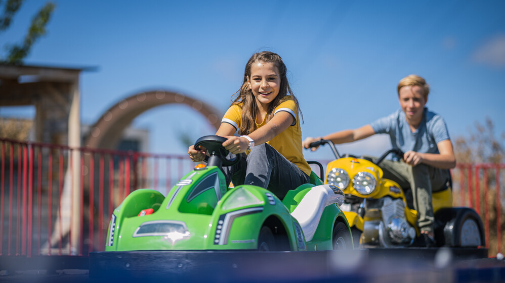 Ein M&auml;dchen und ein Junge fahren hintereinander auf der E-Kartbahn.